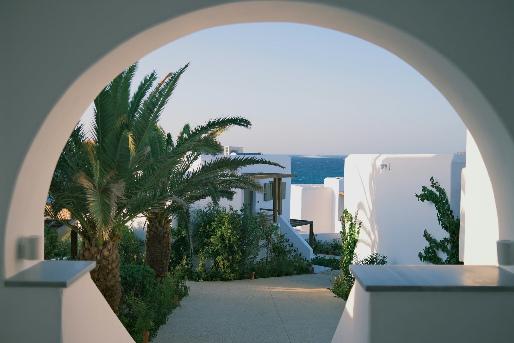 Cour méditerranéenne baignée de lumière, palmiers et murs blancs ouvrant sur la mer